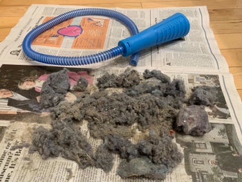 A reviewer photo of the vacuum attachment sitting on a laid-out newspaper next to a large pile of dust 
