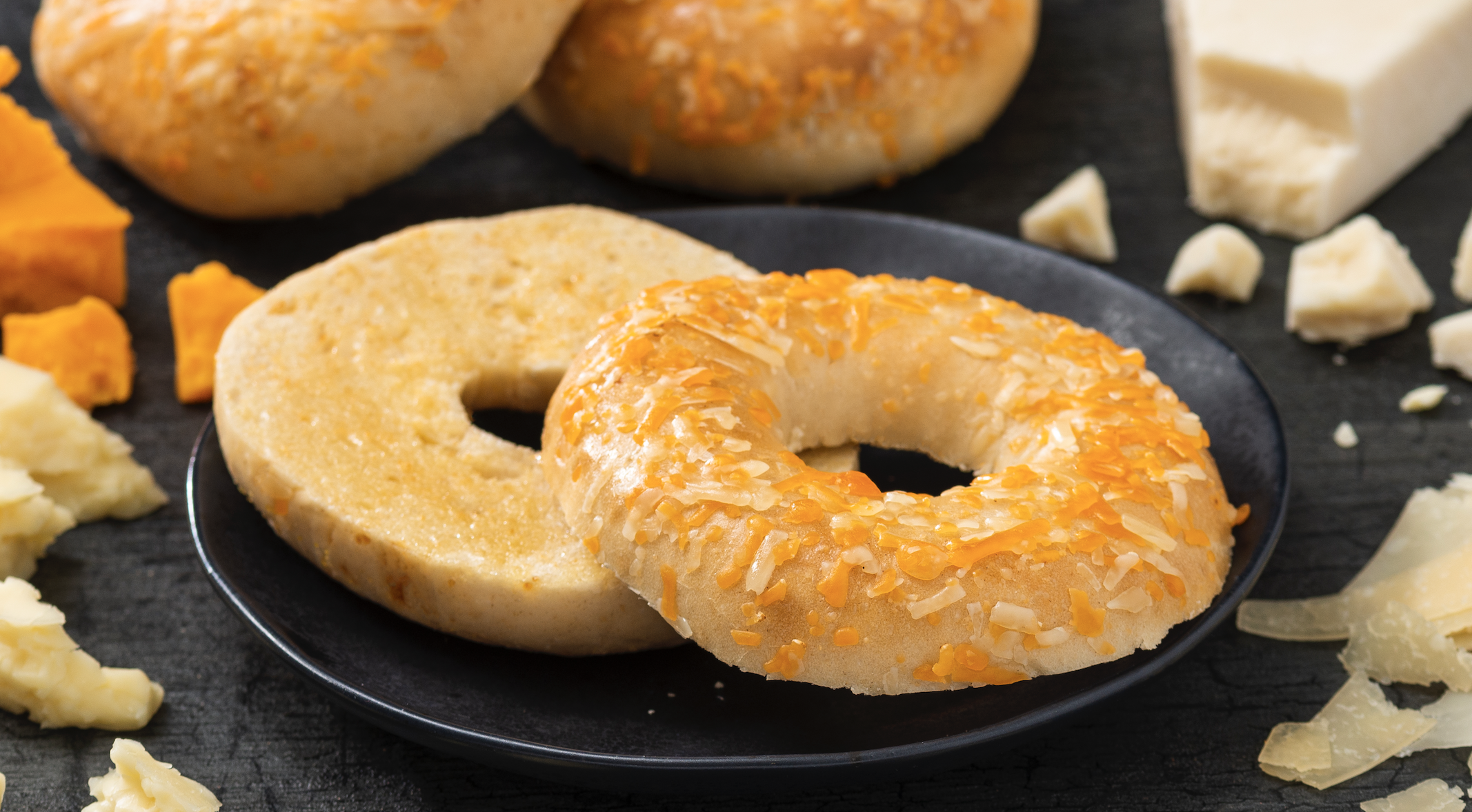 A photo of Four Cheese bagel on a blue plate surrounded by cheese and more bagels.