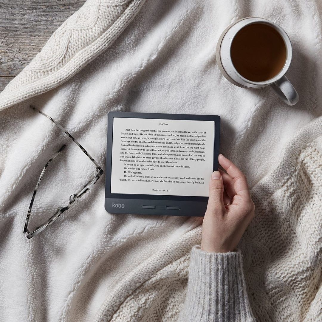 A person holding the e-reader while curled up in a blanket