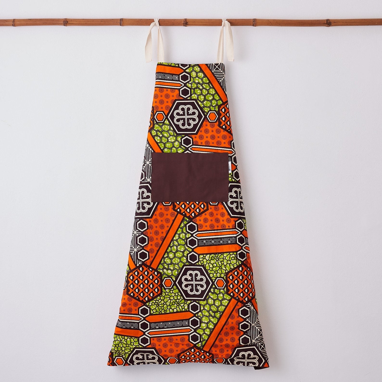 The graphic print apron in orange, purple, and yellow with purple front pocket and beige neck ties
