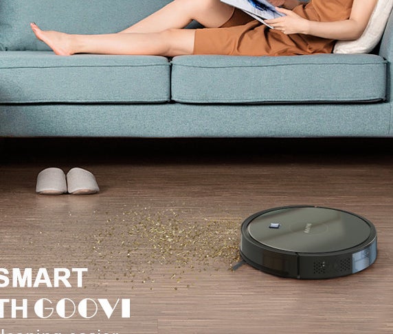 A robotic vacuum cleaning up a mess beside a person lounging on a couch