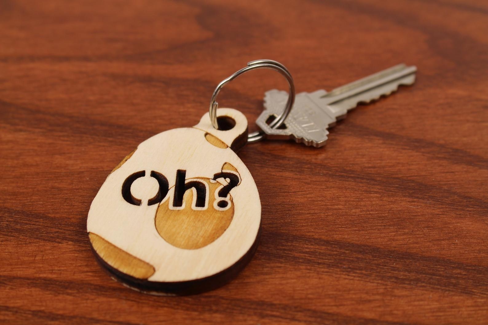 a wooden egg keychain with the word &quot;oh?&quot; etched onto it