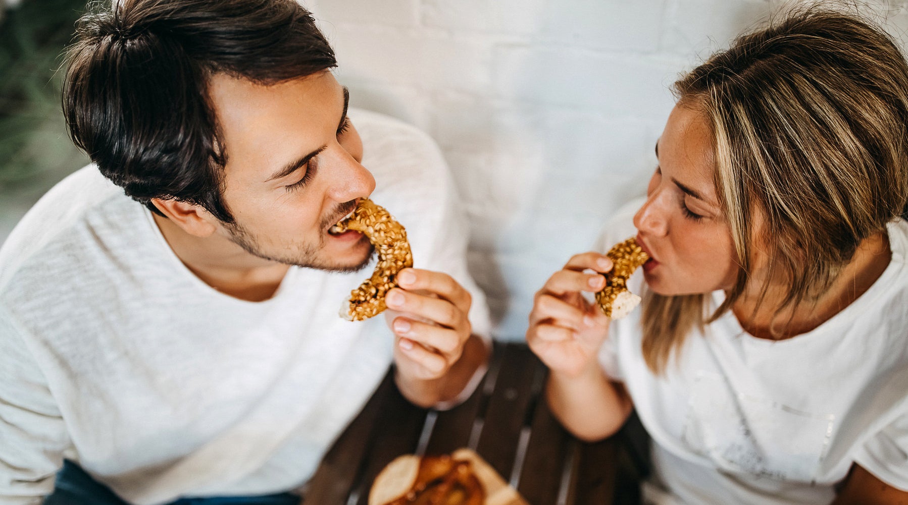 A photo of a man and a woman from above eating a  bagel.