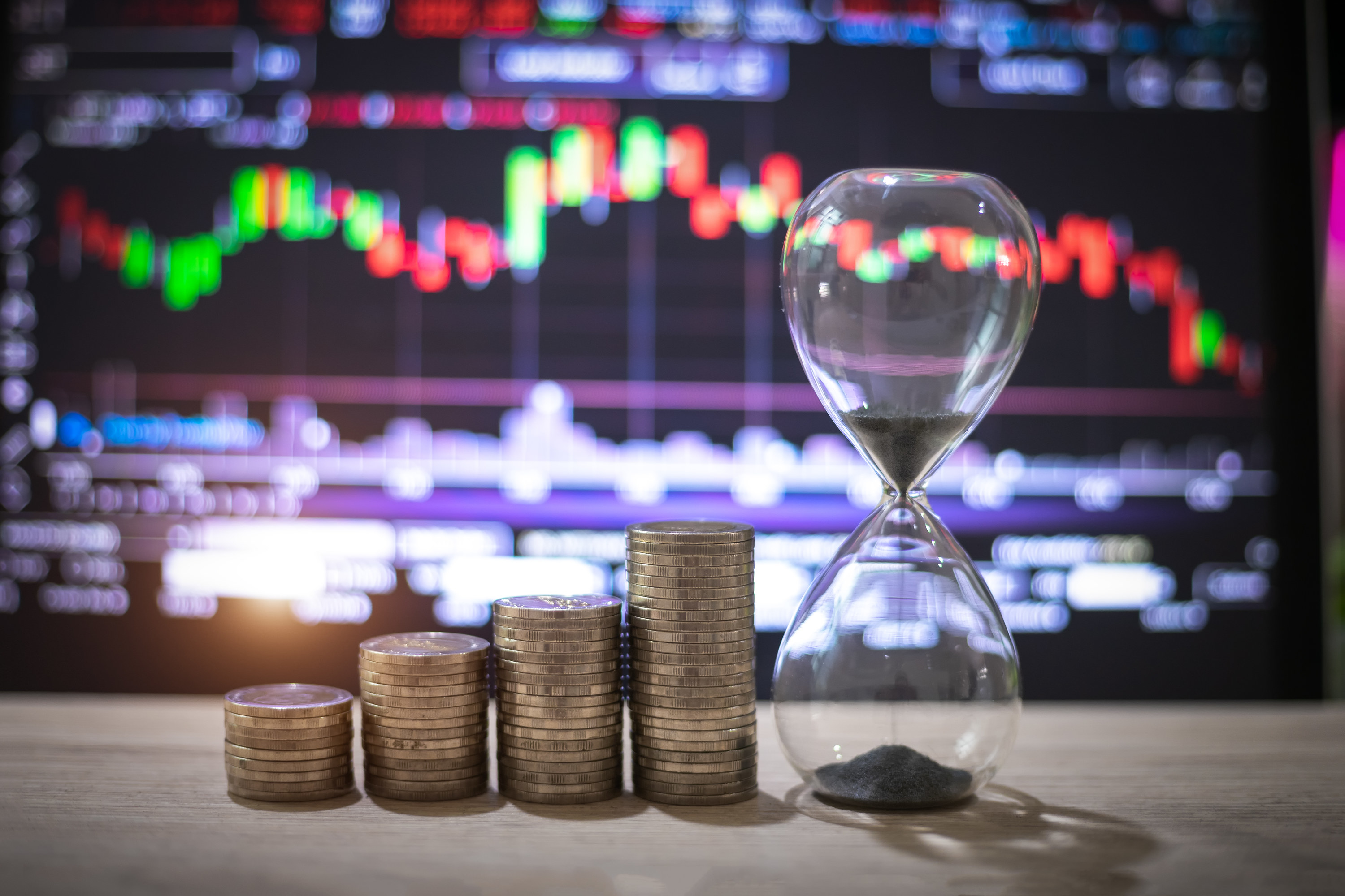 Stack of coins and an hourglass in front of a stock ticker