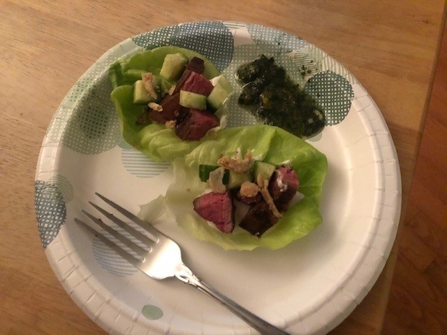 Plate with two steak-filled lettuce cups, a fork, and a green dipping sauce