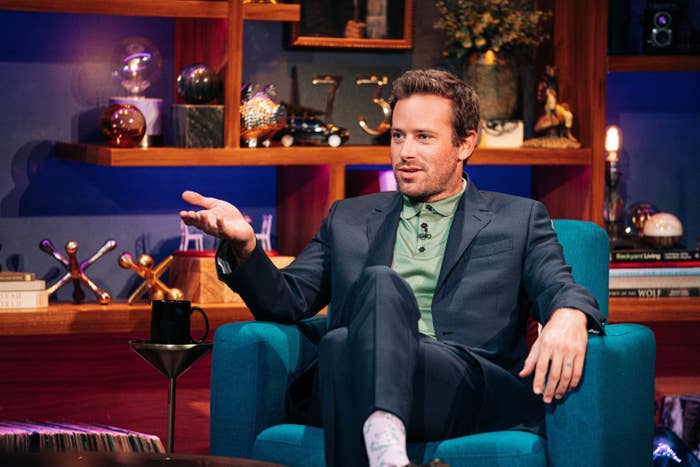 Hammer sits on a chair with his hand raised while wearing a dark blue suit and a green polo on The Late Late Show with James Corden