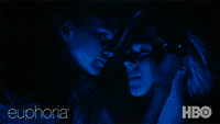 Two women stare at each other in the dark as lights shine on their faces. 