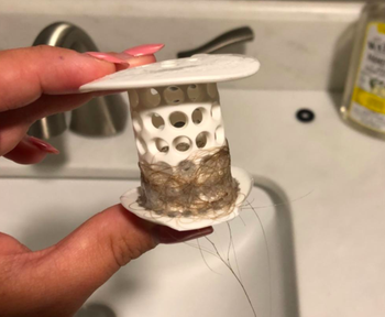 A reviewer holding the TubShroom after taking it out of the drain, and it has hair on it