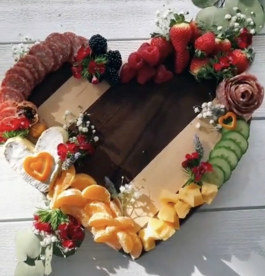 A heart shape wooden board filled with fruit, cheese and meat