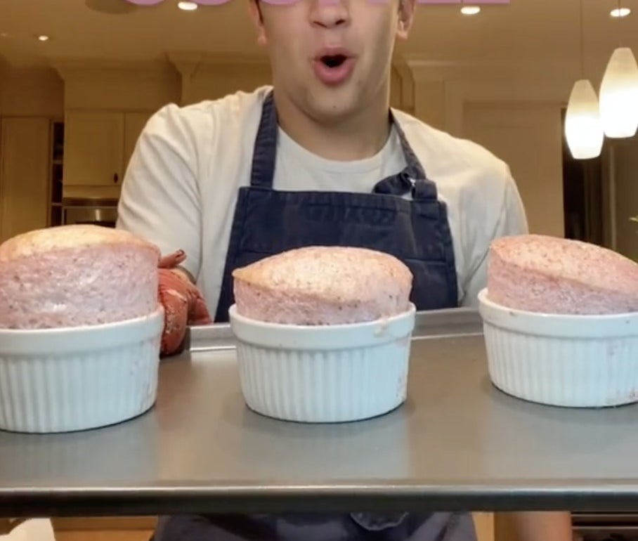 A chef holds up a tray with three pink soufflés