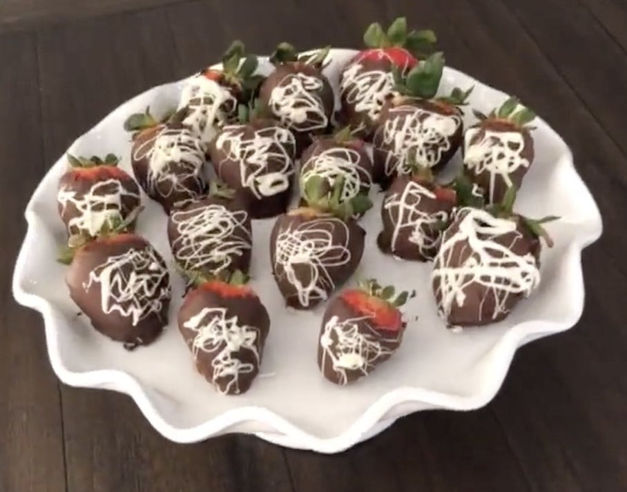 A plate filled with strawberries dipped in chocolate with a white chocolate drizzle