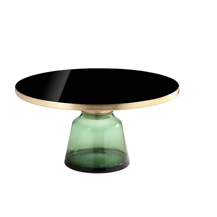 A pedestal coffee table with a brushed gold and glass top and a sculpted translucent base made of green glass