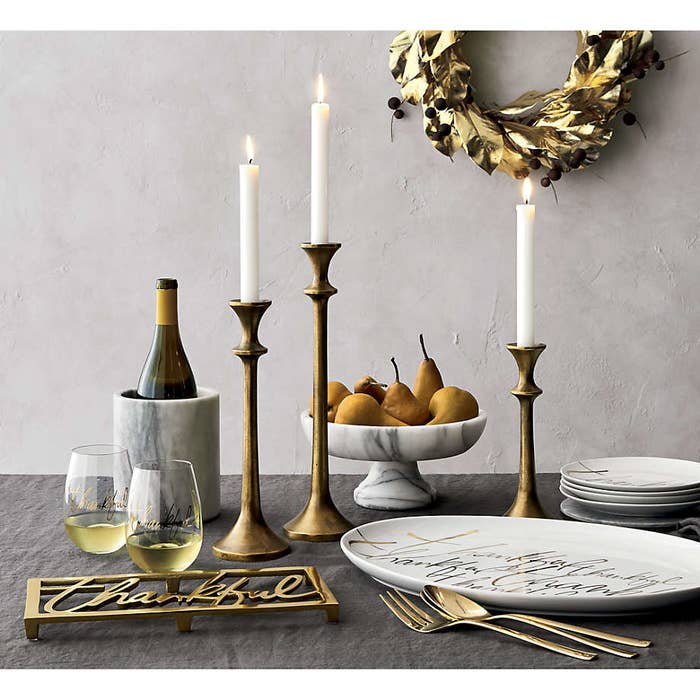 Brushed brass tapered candlesticks of varying height on a dressed table with marble and gold dish-ware