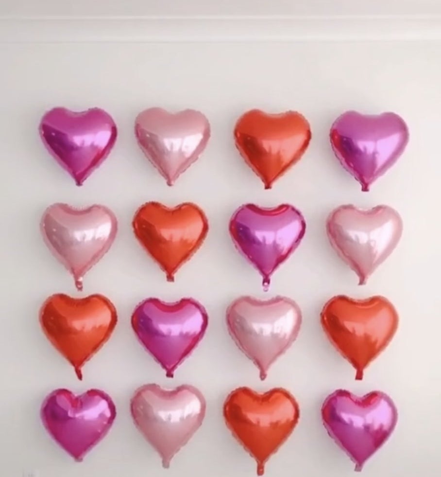 A wall filled with a square of heart shaped balloons in various pink shades