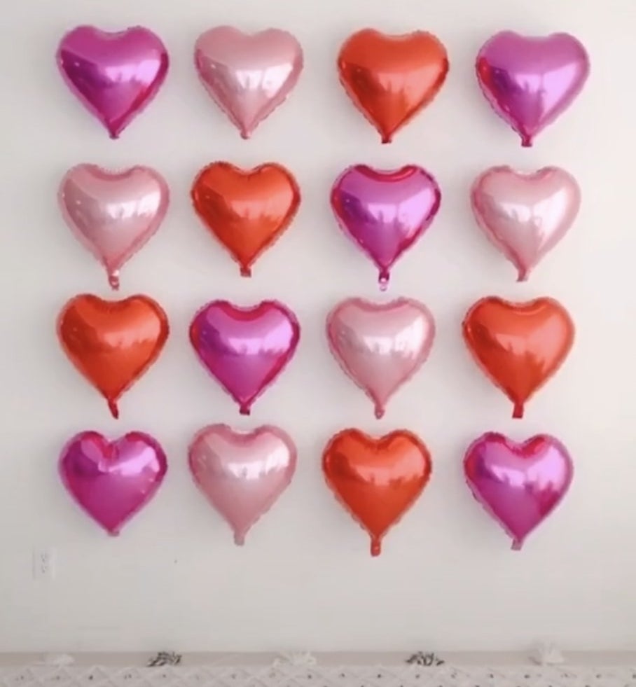 A wall filled with a square of heart shaped balloons in various pink shades