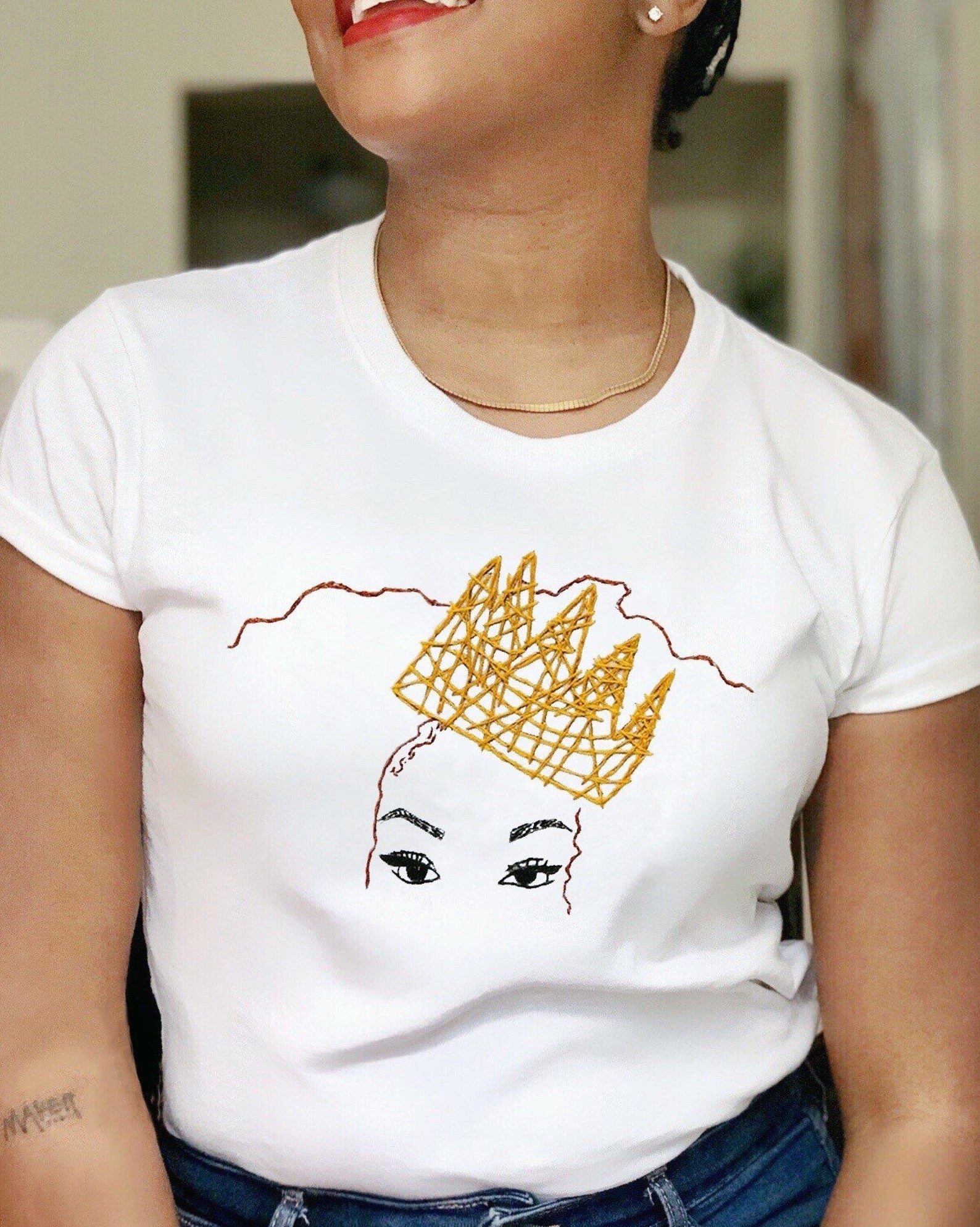 model wearing a t-shirt with a gold embroidered crown over a face just showing eyes and very fleeky eyebrows