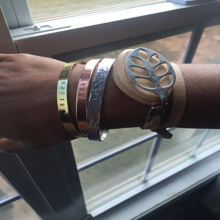 person's wrist with three of the bracelets on which are silver, gold, and brass wit an engraving on them