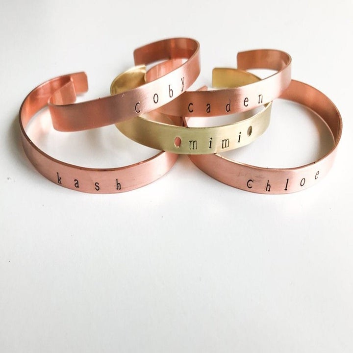 a pile of about five bracelets that are skinny and have an open space for the cuff style. They're gold or brass and each has one name engraved on them.
