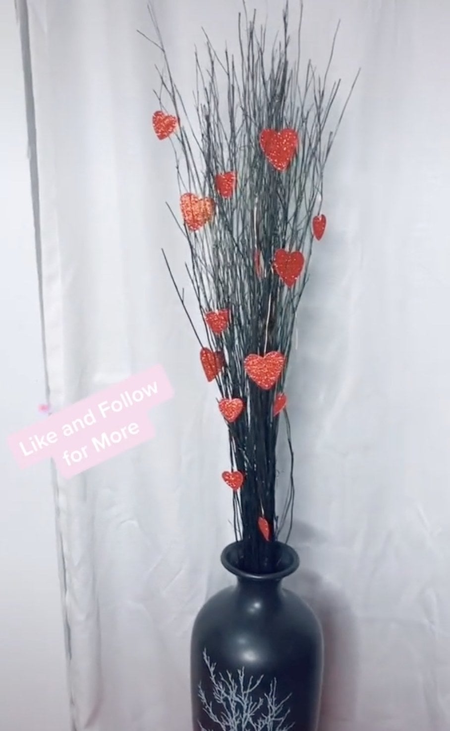 A black vase filled with decorative sticks and hearts