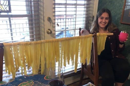 Stick of drying pasta next to woman holding a wine glass