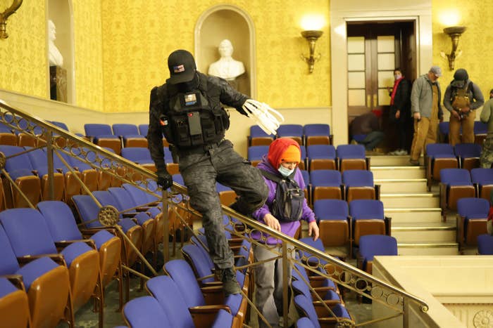 A man in tactical gear with a hat low over his head hops over a railing inside the Senate