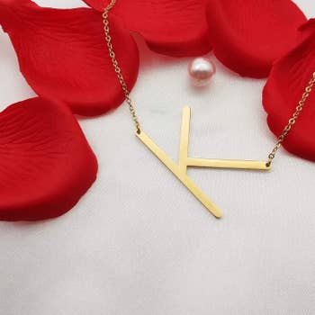 K initial necklace placed on white background with rose petals