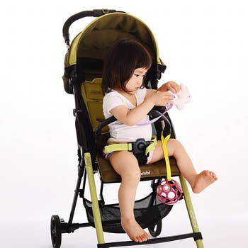 Child playing with toy while another is hanging from their stroller, not falling thanks to the strap it's attached to 