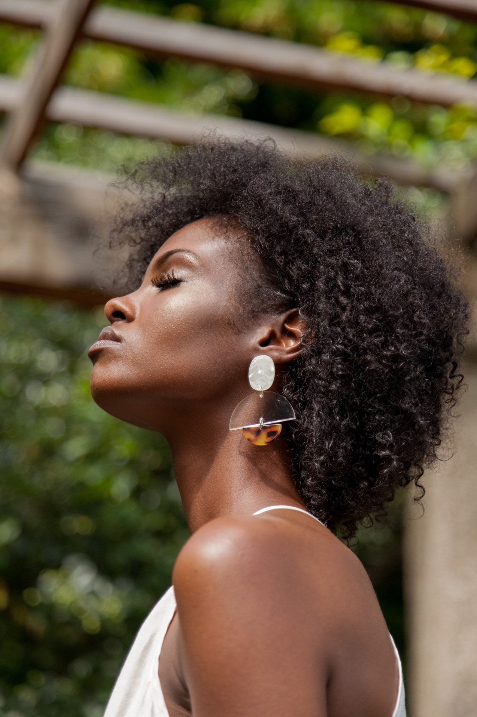 model wearing dangling earrings with one circular ivory portion, a clear half circle hanging underneath, and a smaller tortoiseshell half-circle underneath that