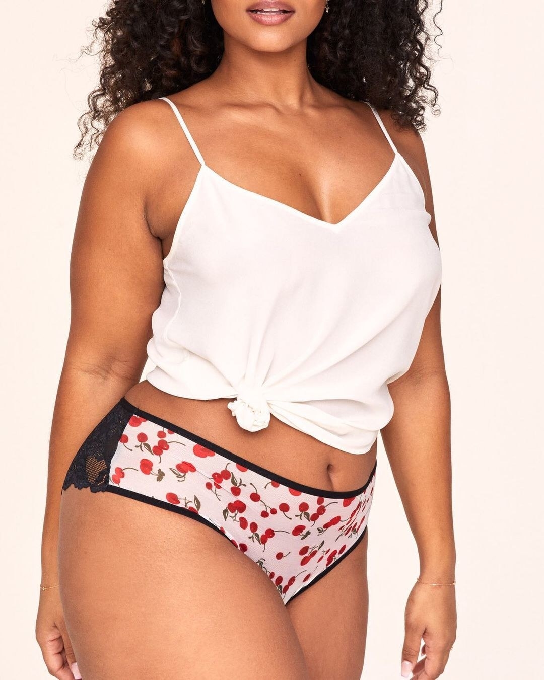 a model wearing pink underwear with a cherry print and black lace detail