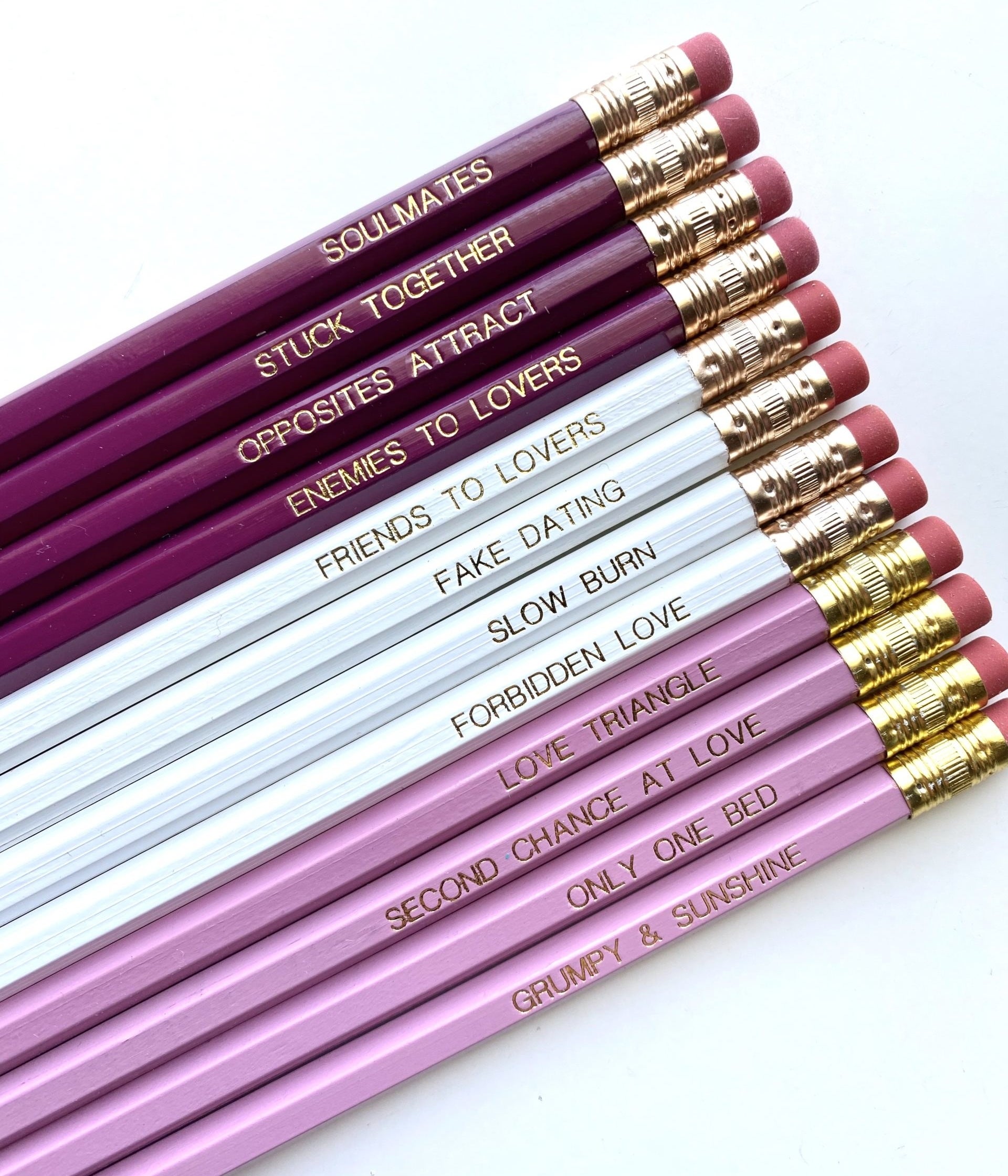 The pink, purple, and white pencils printed with: soulmates, stuck together, opposites attract, enemies to lovers, friends to lovers, fake dating, slow burn, forbidden love, love triangle, second chance at love, only one bed, and grumpy &amp;amp; sunshine