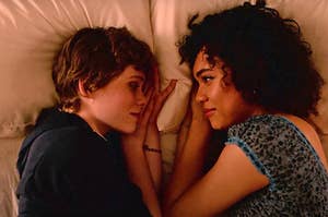 Sydney and Dina from "I Am Not Okay With This" lie on the bed across from each other and exchange loving glances