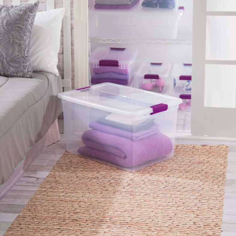 the clear bin with purple latches storing a blanket and sheet set in a bedroom 