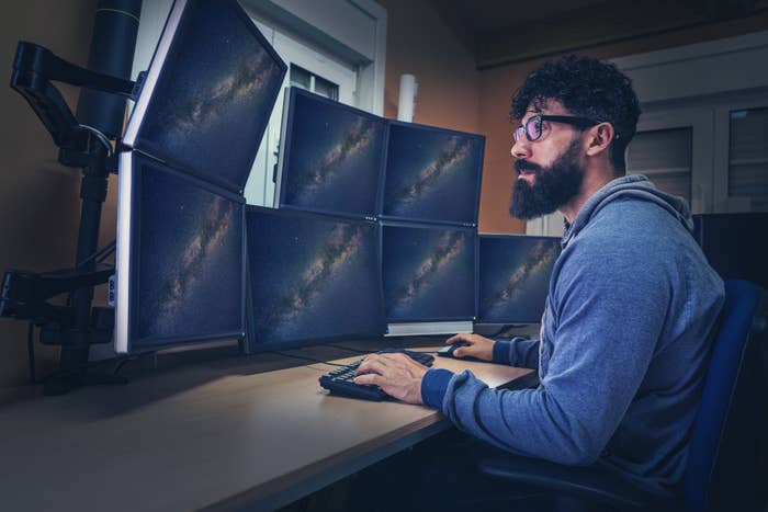 A man sitting behind a desk with a bunch of screens