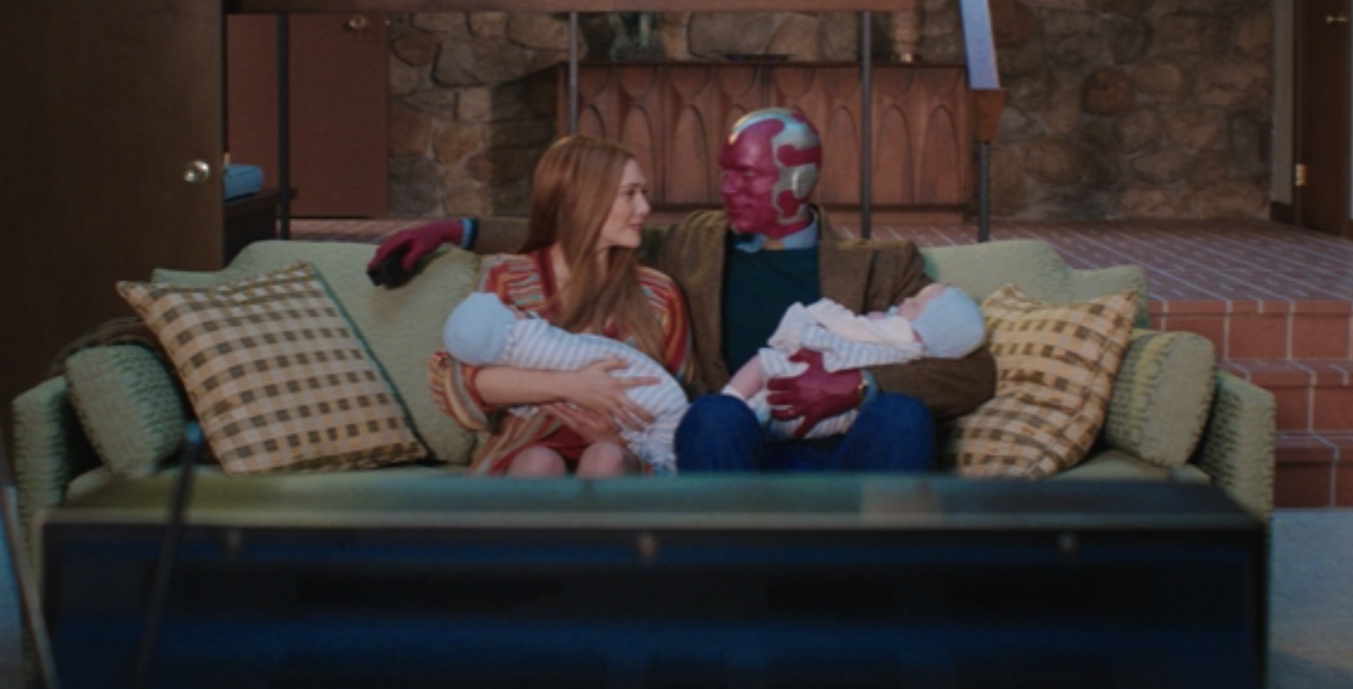 Vision and Wanda sitting on their couch holding their twin boys