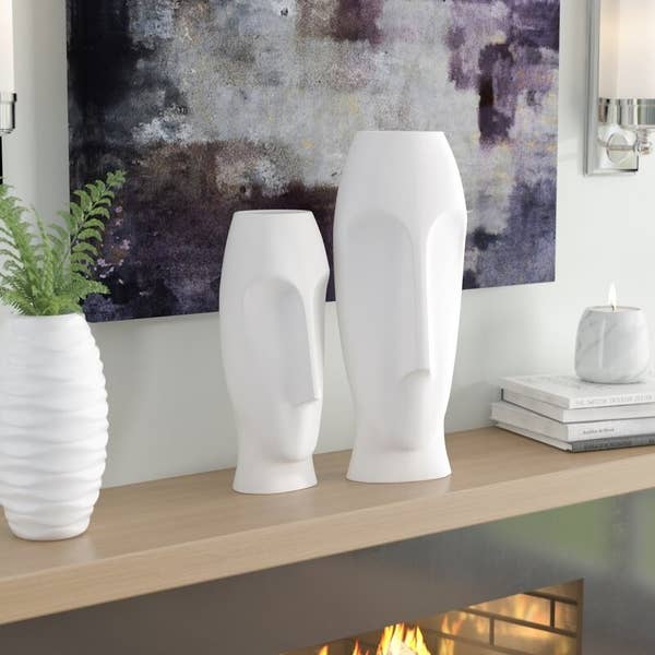 white face vases on a tan shelf with other white decor and a piece of gray and purple art