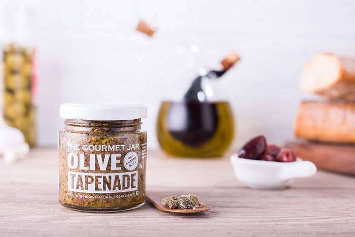 Jar of the olive spread surrounded by other condiments and a spoon