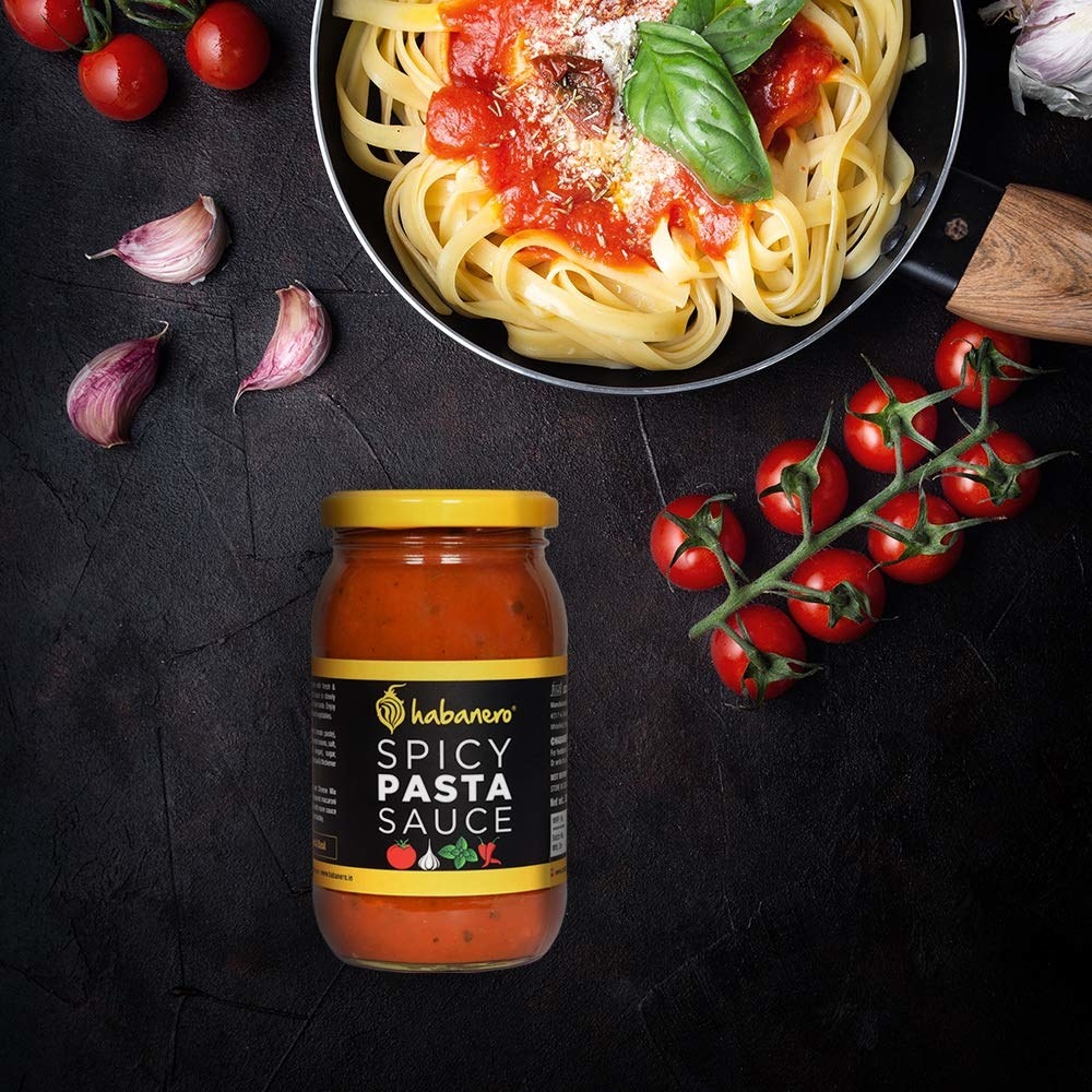 A jar of spicy pasta sauce with tomatoes, onion and a bowl of pasta 