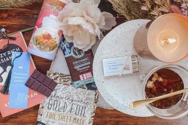 Books, herbal tea, chocolate bars, a candle, and dried flowers on a table top