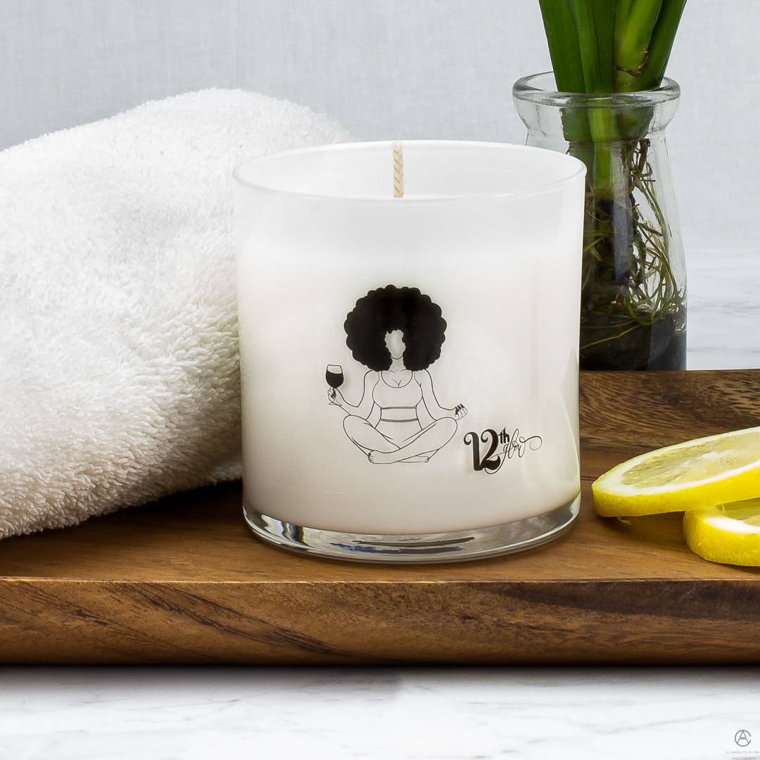 the lemongrass candle on with a drawing of a figure holding a glass of wine and sitting cross-legged 