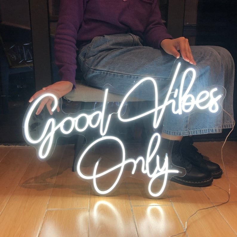 a model sitting next to the white neon "good vibes only" sign