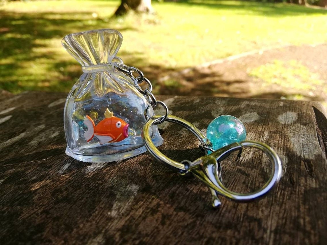 a keychain with a charm that looks like a plastic bag with tiny magikarp inside 