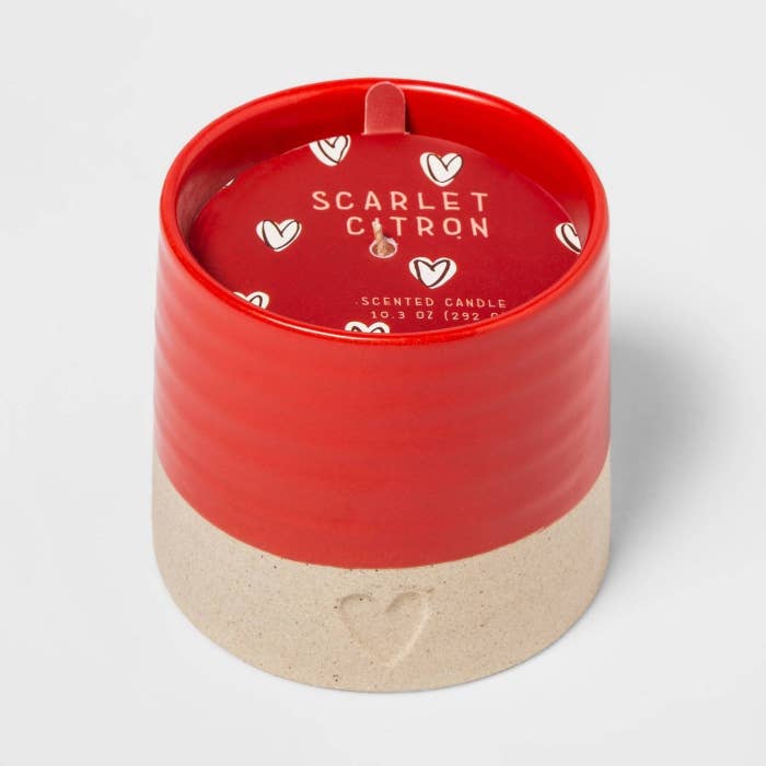 The candle, which comes in a circular ceramic holder that is red on top and beige on the bottom, with a small heart printed in the base