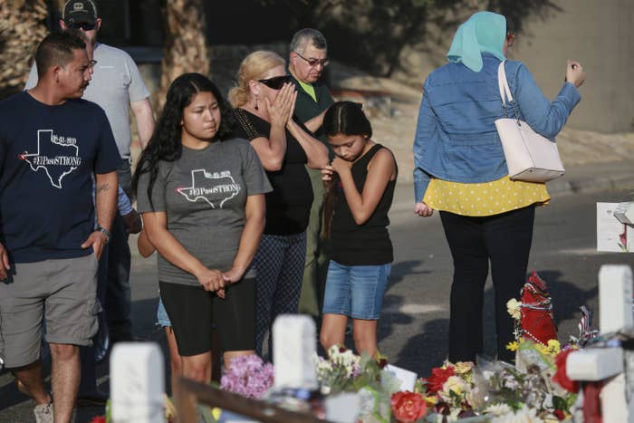 A group of people gathers around a memorial with flowers