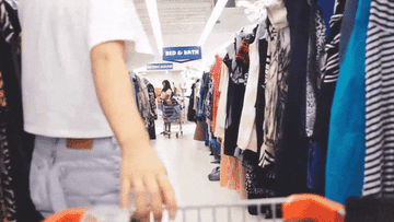A person dragging their shopping cart leisurely through a clothes aisle