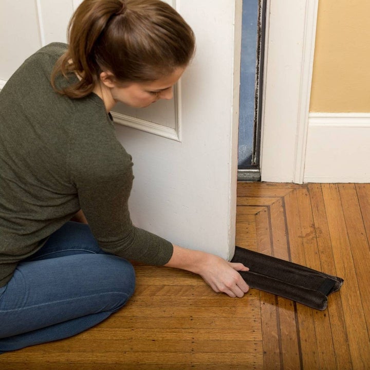 person applies black draft protector on the bottom of a door