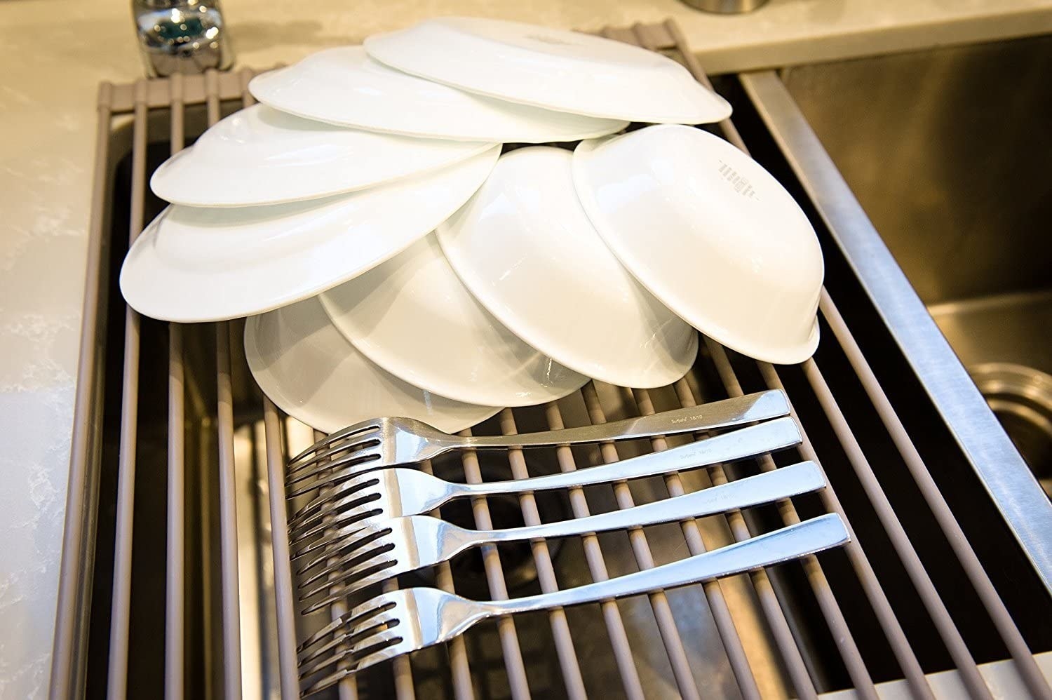 The roll out drying rack with plates, bowls, and forks drying over a sink