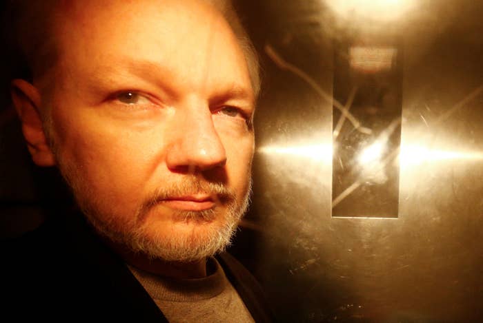 A close-up of Julian Assange's face with the camera's flash reflected in the steel door behind him