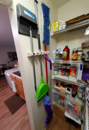 small kitchen pantry with a row of hooks and brooms and mops hanging up on it and out of the way