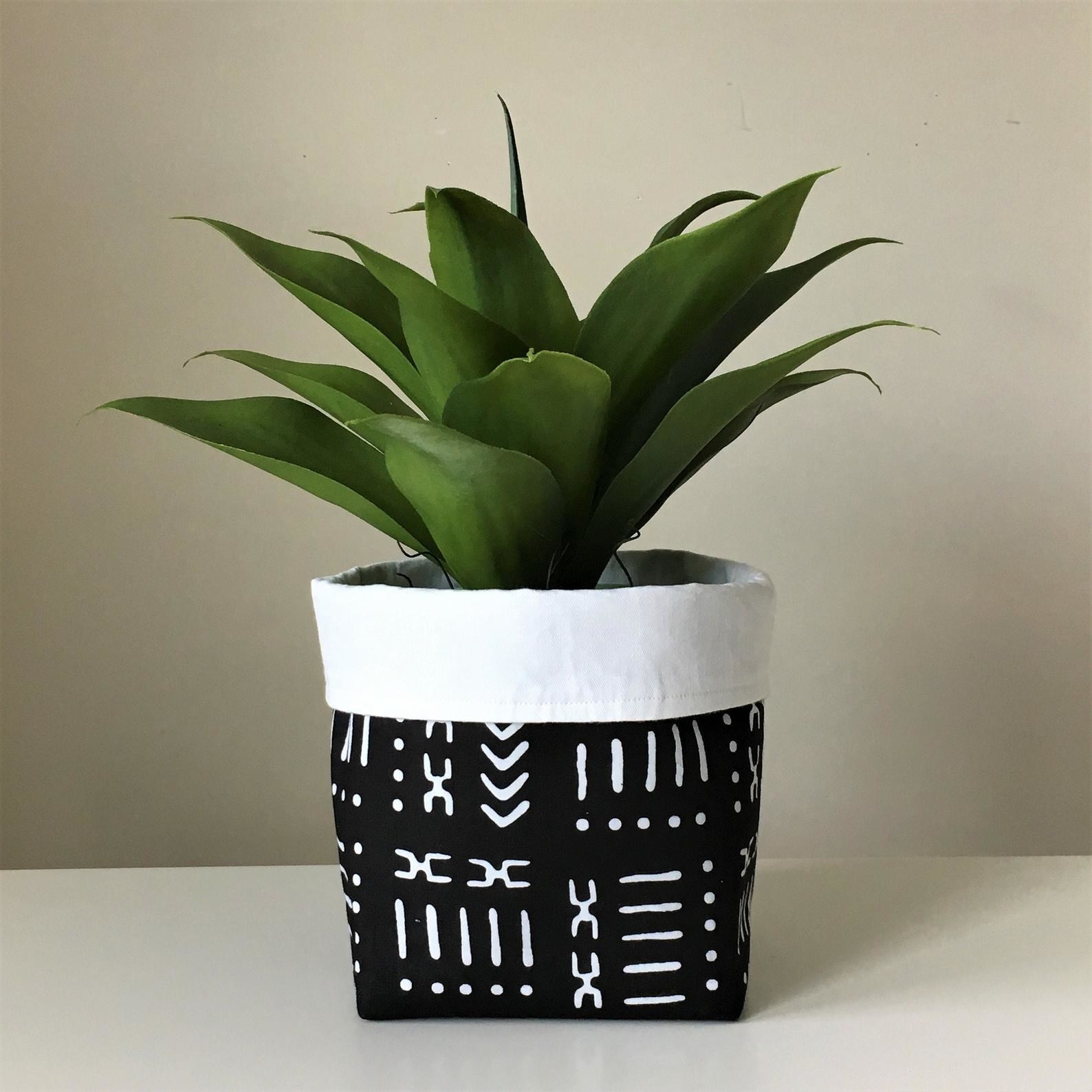 The fabric basket with a plant in it in black with white printed design all over it and the top part folded down to show the other wite side