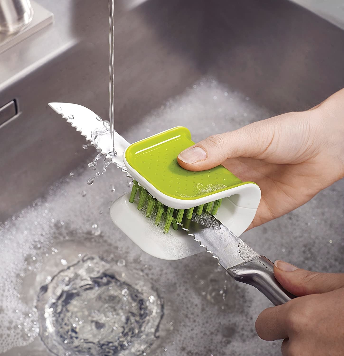 A person using the cutlery brush to wash a serrated knife 